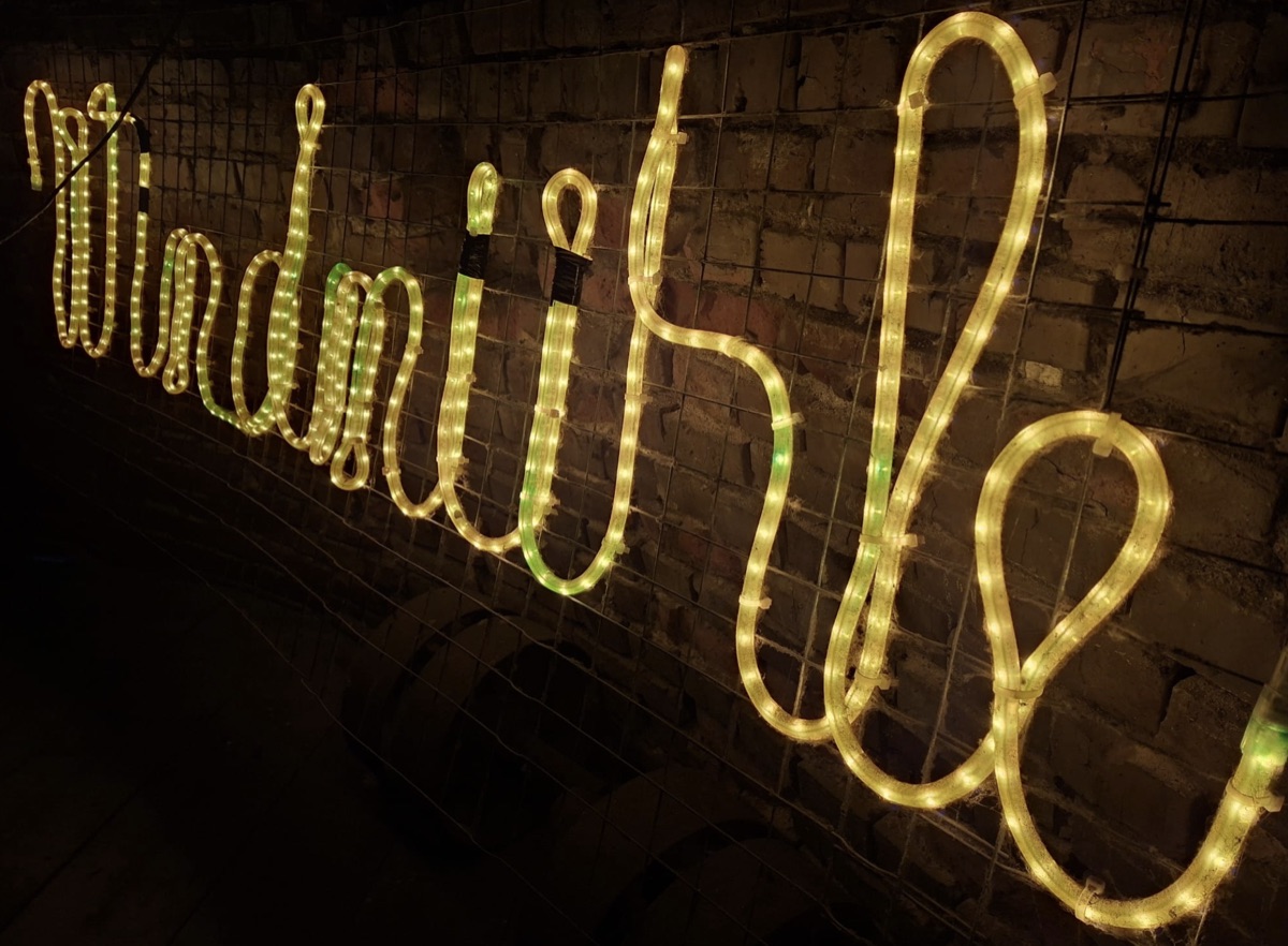 Letrero luminoso Windmühle en el muro de piedra